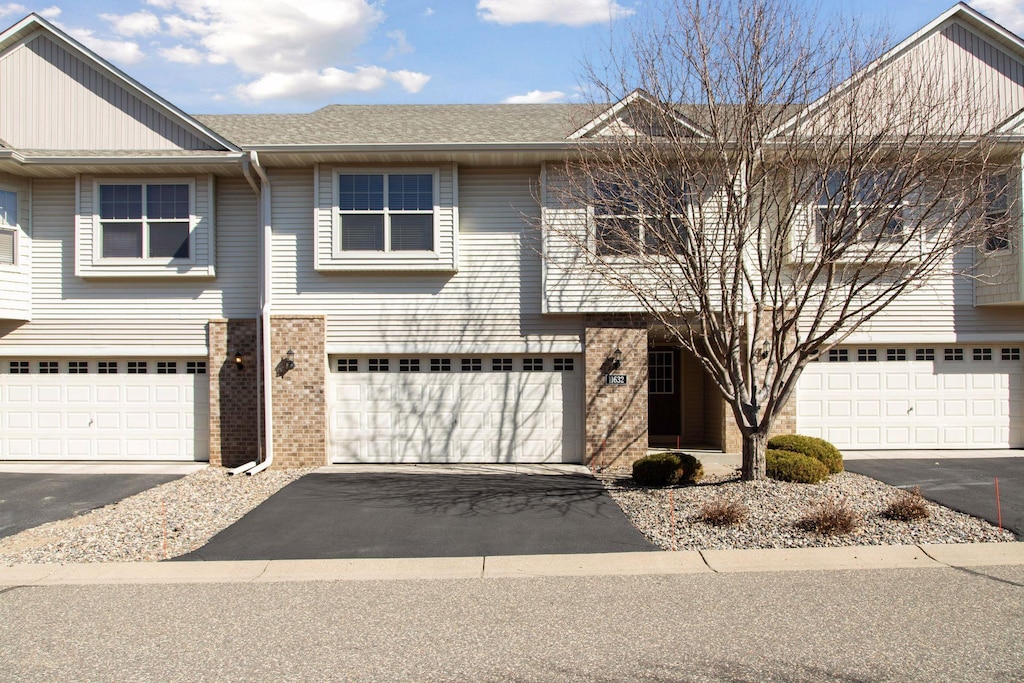 view of property featuring brick siding, a shingled roof, aphalt driveway, and an attached garage