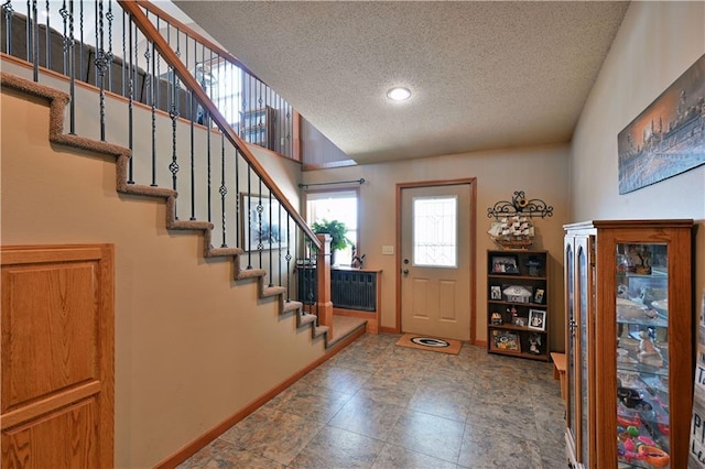 entryway with a textured ceiling, baseboards, and stairs