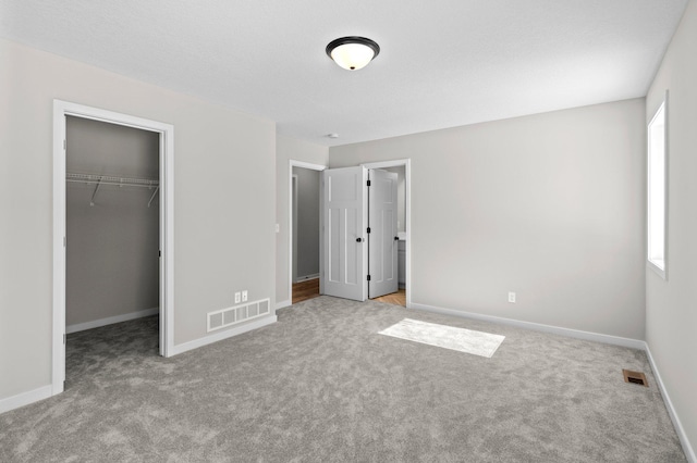 unfurnished bedroom with carpet floors, a walk in closet, and visible vents