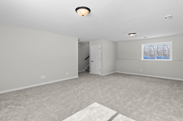 empty room featuring stairs, a textured ceiling, carpet flooring, and baseboards