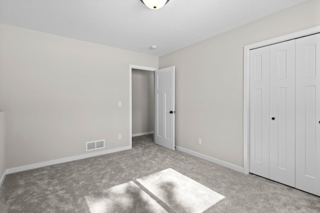 unfurnished bedroom featuring carpet, a closet, visible vents, a textured ceiling, and baseboards