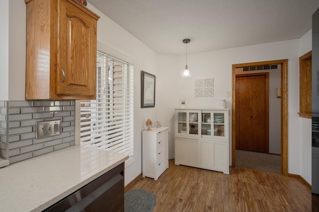 kitchen with a textured ceiling, wood finished floors, baseboards, tasteful backsplash, and decorative light fixtures