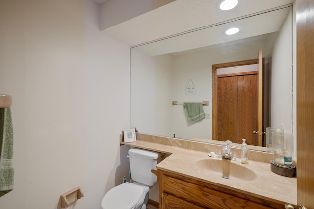 half bathroom featuring recessed lighting, vanity, and toilet