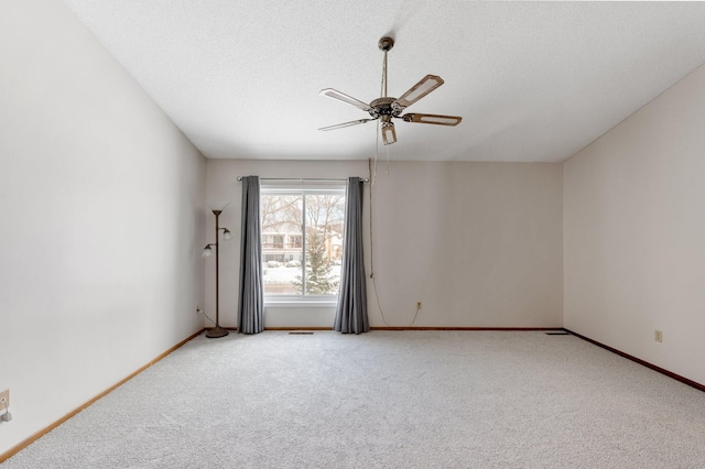 spare room with a textured ceiling, carpet flooring, a ceiling fan, and baseboards