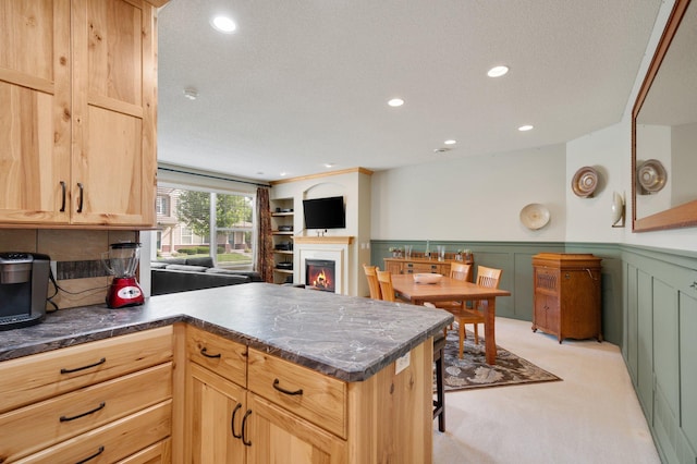 kitchen with light carpet, a peninsula, a wainscoted wall, a lit fireplace, and dark countertops