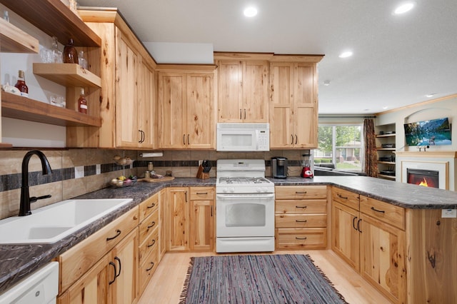 kitchen featuring white appliances, dark countertops, a peninsula, light brown cabinetry, and a sink