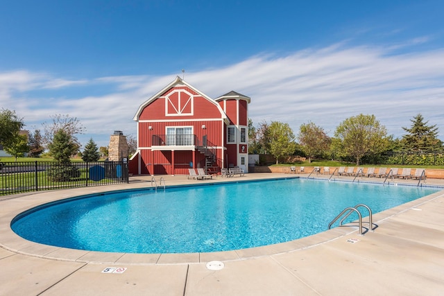 community pool featuring a barn, a patio area, and fence