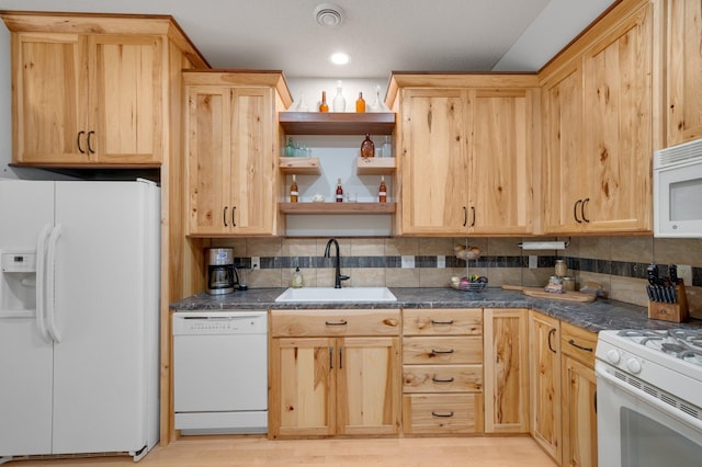 kitchen with dark countertops, white appliances, a sink, and light brown cabinetry