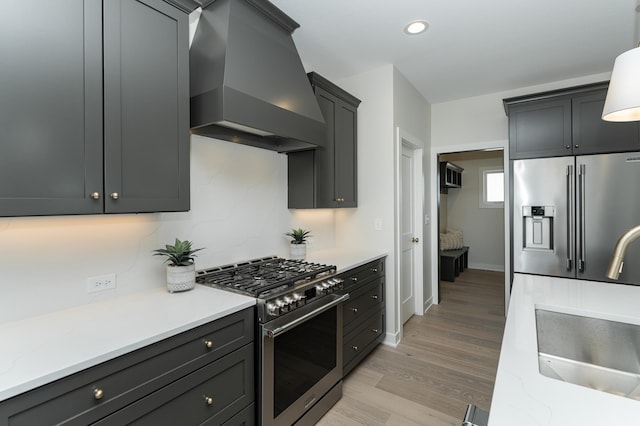 kitchen with light wood-type flooring, wall chimney range hood, light stone counters, and premium appliances