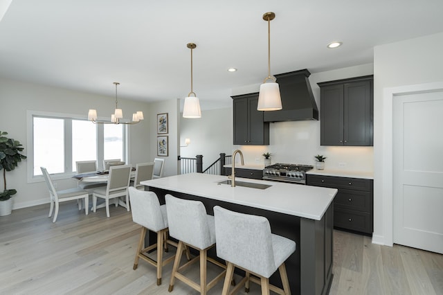 kitchen featuring custom range hood, high end stainless steel range oven, light countertops, light wood-type flooring, and a sink