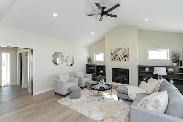 living room featuring baseboards, a glass covered fireplace, vaulted ceiling, light wood-style floors, and recessed lighting