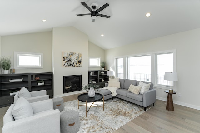 living area with light wood finished floors, lofted ceiling, recessed lighting, a glass covered fireplace, and baseboards