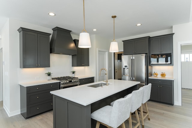 kitchen with premium appliances, light countertops, a sink, and wall chimney range hood