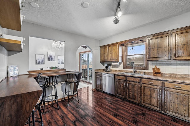 kitchen with dark wood-style floors, a sink, dishwasher, a kitchen breakfast bar, and tasteful backsplash