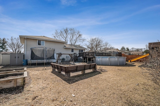 rear view of house featuring a storage unit, an outbuilding, a deck, a trampoline, and a fenced in pool