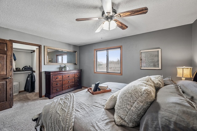 bedroom with a walk in closet, a textured ceiling, a closet, carpet floors, and ceiling fan