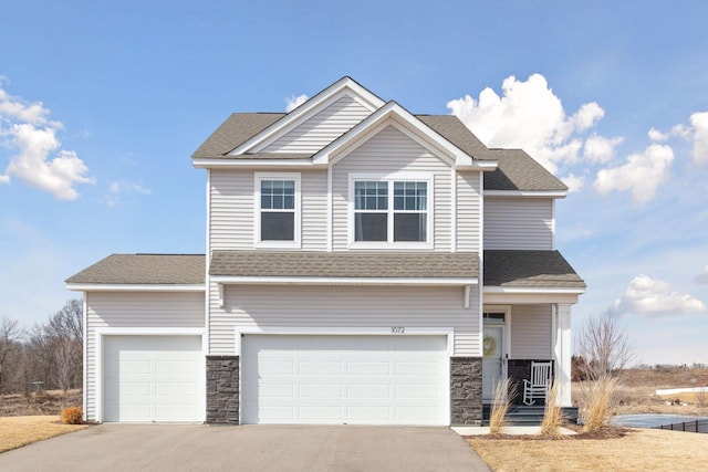 view of front facade with stone siding, driveway, a shingled roof, and a garage