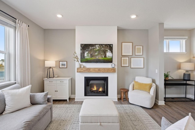 living room with a textured ceiling, a glass covered fireplace, wood finished floors, recessed lighting, and baseboards