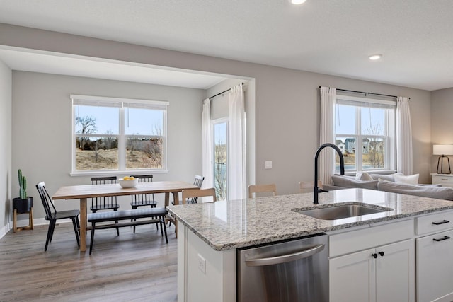 kitchen with a sink, light wood-type flooring, light stone countertops, and stainless steel dishwasher