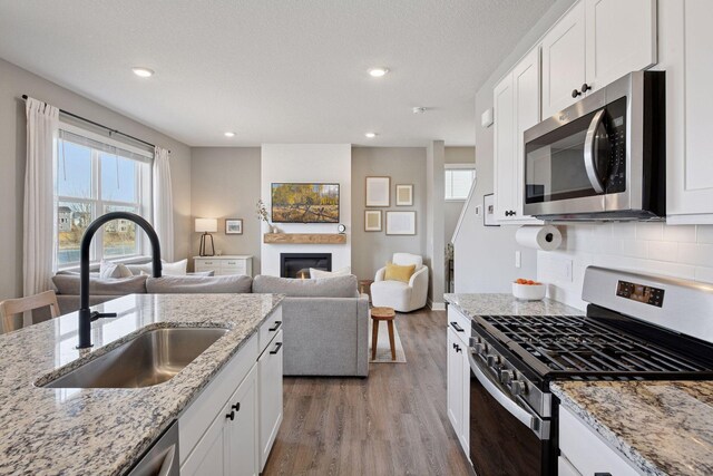 kitchen featuring a sink, a glass covered fireplace, appliances with stainless steel finishes, light wood finished floors, and decorative backsplash