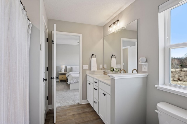 bathroom with toilet, a sink, wood finished floors, ensuite bath, and double vanity