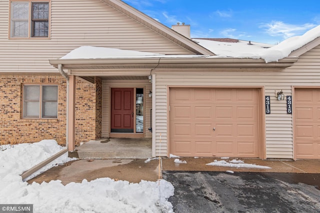 snow covered property entrance with brick siding and a chimney