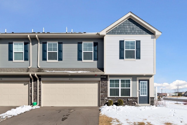 multi unit property featuring a garage, driveway, and stone siding