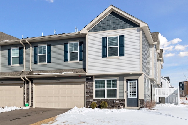 view of property with an attached garage, stone siding, central AC, and roof with shingles