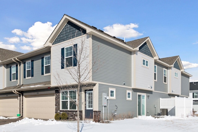 view of snowy exterior featuring an attached garage, stone siding, and cooling unit