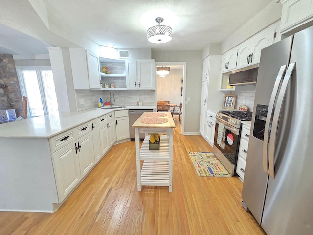 kitchen featuring open shelves, light countertops, light wood-style flooring, appliances with stainless steel finishes, and a peninsula