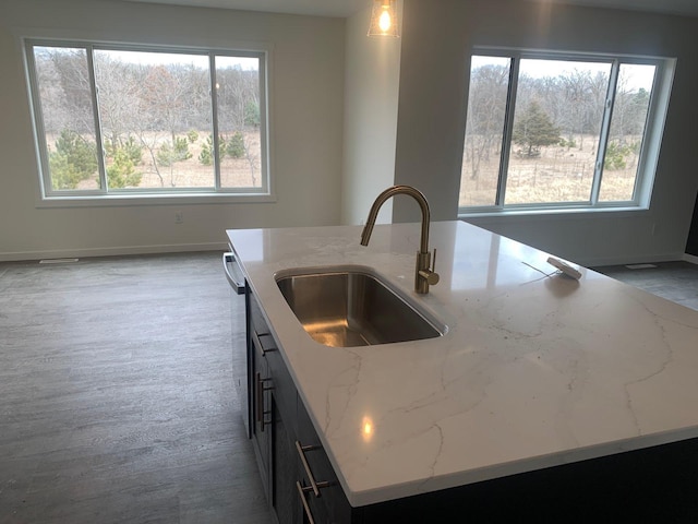 kitchen with light stone counters, baseboards, a sink, and an island with sink