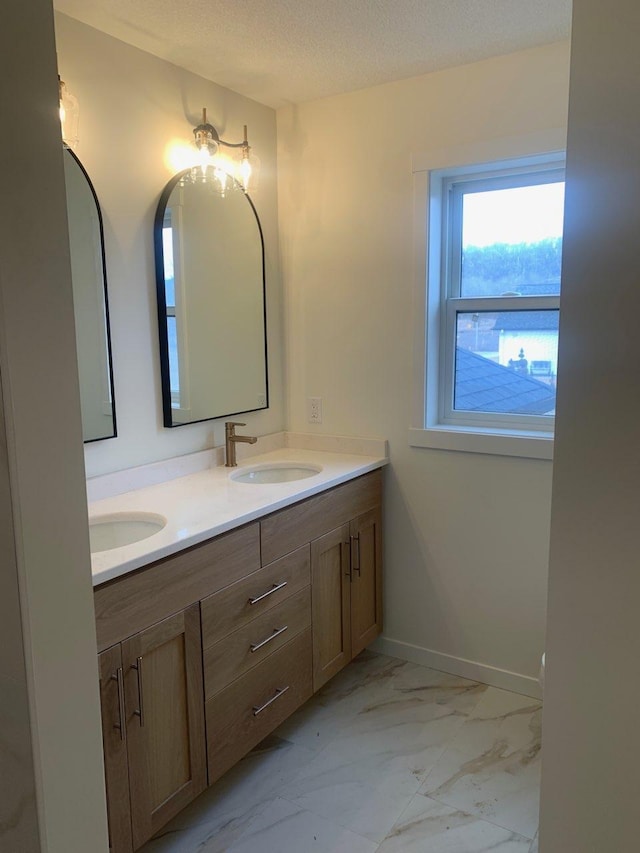 full bath featuring marble finish floor, double vanity, a sink, a textured ceiling, and baseboards