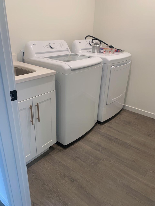 clothes washing area with cabinet space, dark wood finished floors, washer and clothes dryer, and baseboards