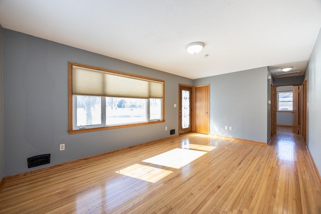 spare room featuring light wood-type flooring, visible vents, and a wealth of natural light