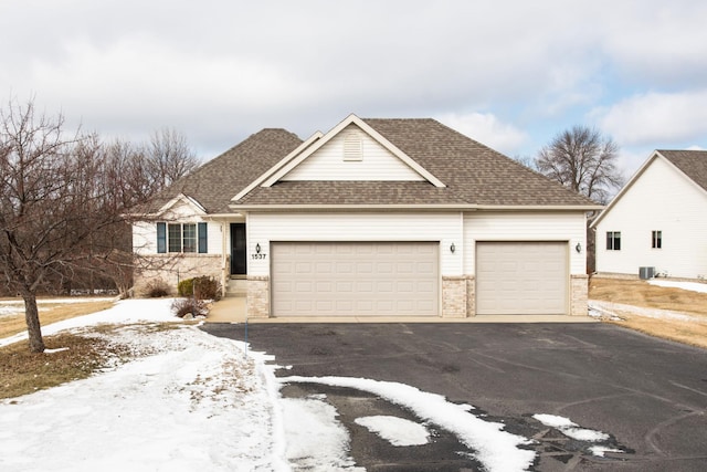 ranch-style house featuring cooling unit, driveway, roof with shingles, an attached garage, and brick siding