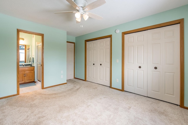 unfurnished bedroom with ensuite bath, light colored carpet, two closets, and baseboards