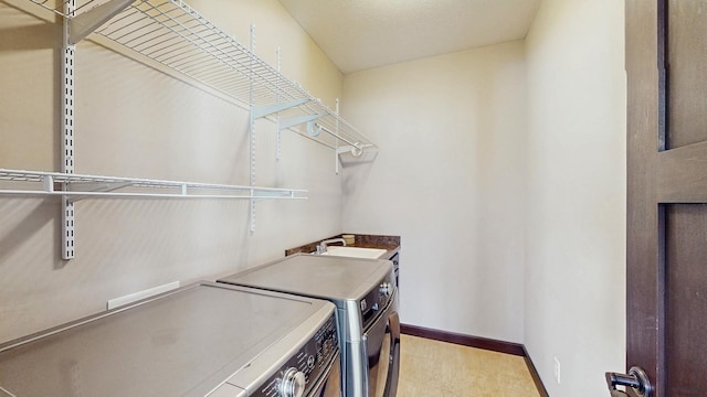 clothes washing area featuring laundry area, a sink, baseboards, and separate washer and dryer