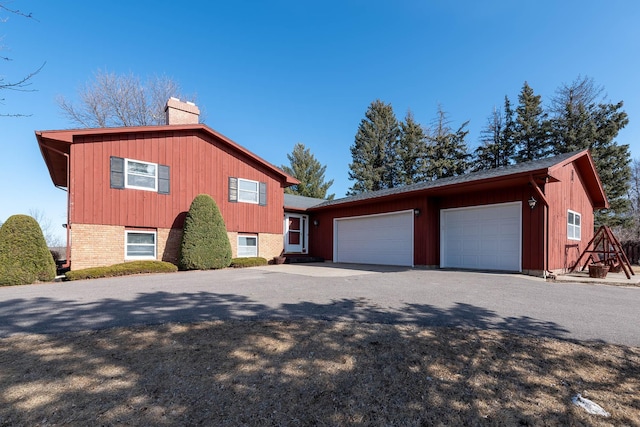 view of side of property featuring a garage, driveway, brick siding, and a chimney