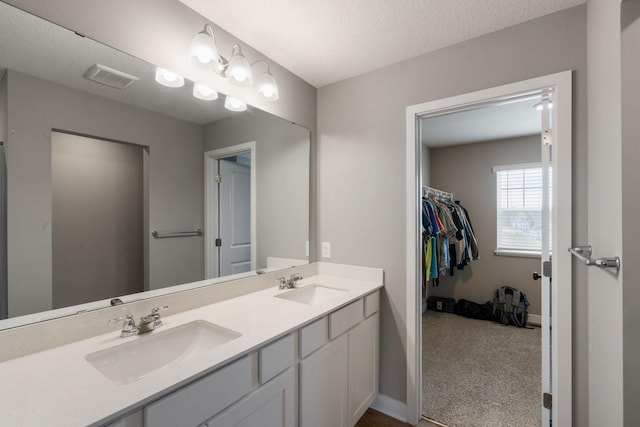 bathroom featuring visible vents, a sink, a textured ceiling, and double vanity