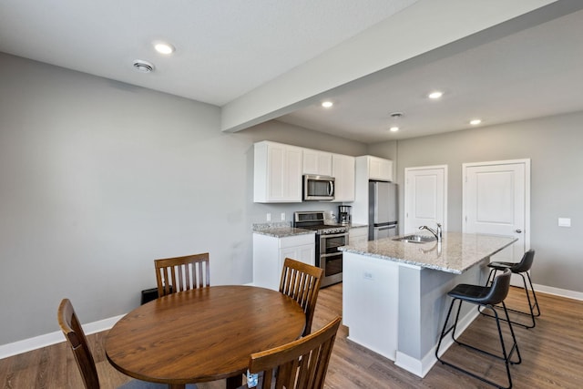 kitchen with appliances with stainless steel finishes, white cabinets, a kitchen island with sink, a sink, and wood finished floors