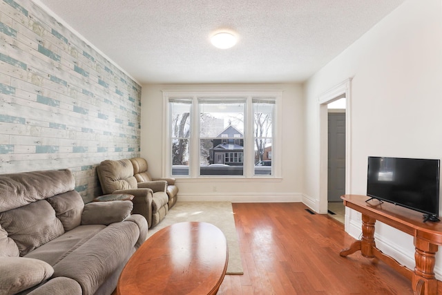 living room with baseboards, a textured ceiling, wood finished floors, and an accent wall