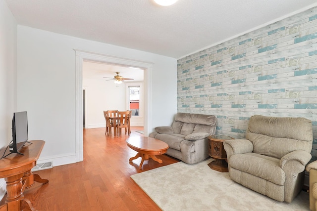 living area with visible vents, an accent wall, baseboards, and wood finished floors