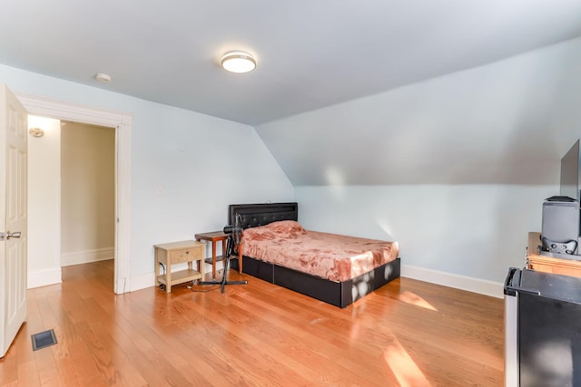 bedroom with light wood finished floors, visible vents, baseboards, and vaulted ceiling