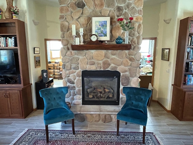 living area featuring baseboards, wood finish floors, and a stone fireplace