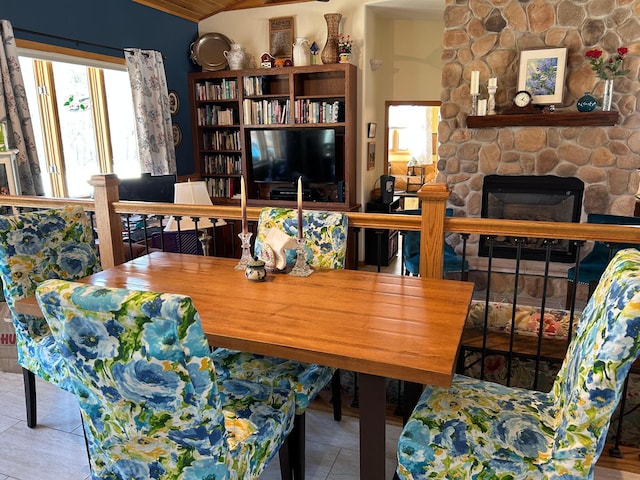 dining room featuring lofted ceiling, tile patterned flooring, and a stone fireplace