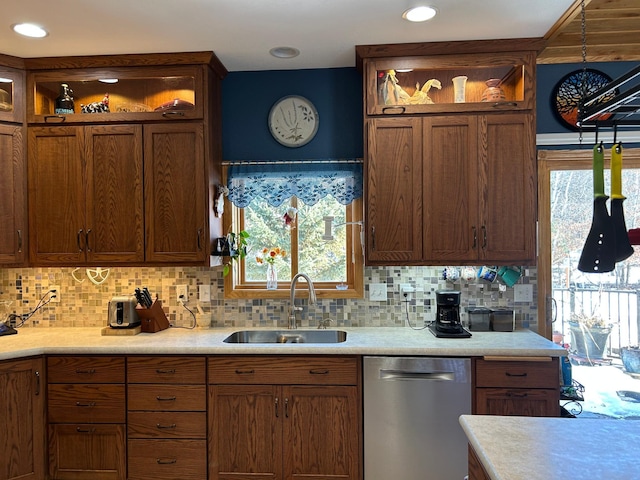 kitchen with light countertops, stainless steel dishwasher, a sink, and decorative backsplash