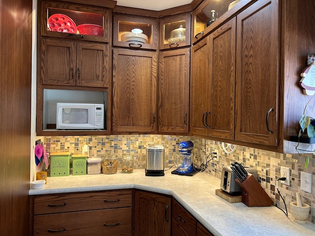 kitchen featuring white microwave, glass insert cabinets, light countertops, and decorative backsplash