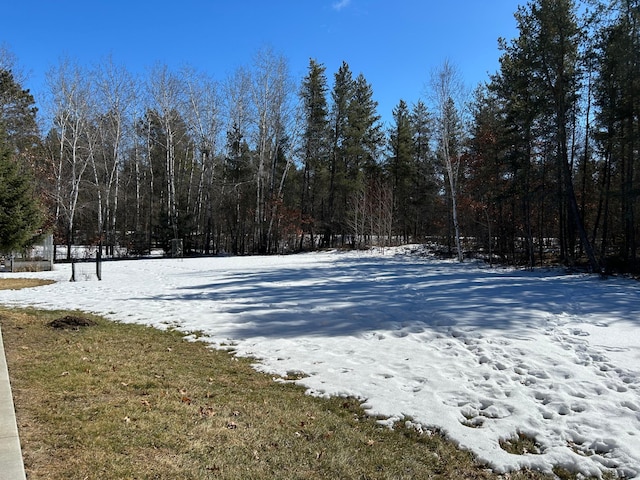 snowy yard featuring a wooded view