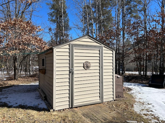 snow covered structure featuring an outdoor structure and a storage unit