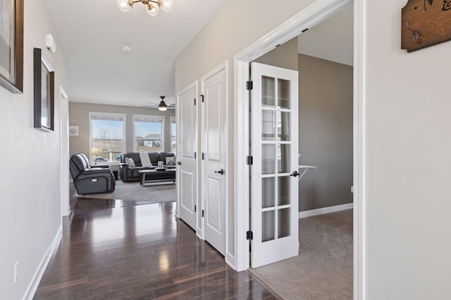 hallway featuring baseboards, dark wood finished floors, and a chandelier